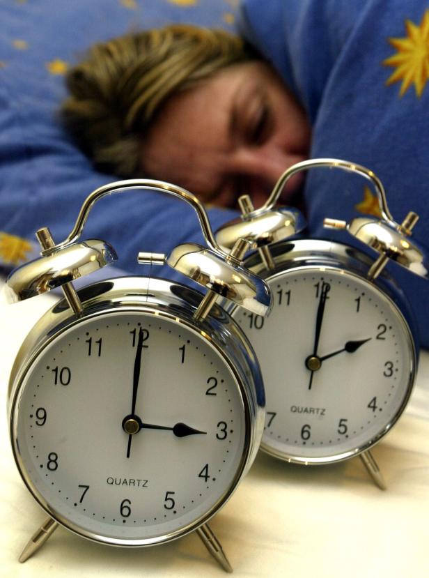 THEMENBILD - UMSTELLUNG AUF SOMMERZEIT Eine schlafende Person liegt im Bett, im Vordergrund zwei Wecker.