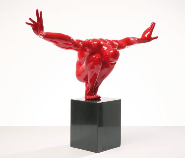 Eine rote Skulptur einer menschlichen Figur in einer dynamischen Pose auf einem schwarzen Sockel.