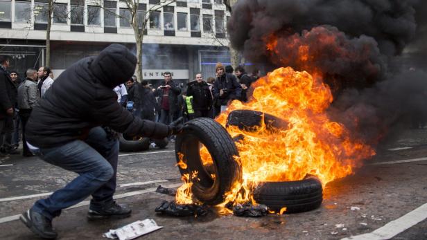 Im März protestierten PSA-Mitarbeiter vom dem Hauptquartier in Paris, in dem sie Reifen in Brand steckten Ein Mann legt einen Reifen auf einen brennenden Stapel Reifen inmitten einer Menschenmenge.