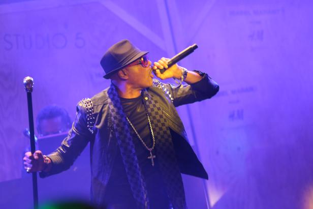 Ein Sänger mit Hut und Sonnenbrille performt auf einer Bühne mit Mikrofon.