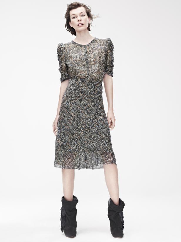 Milla Jovovich trägt ein gemustertes Kleid und Fransenstiefel vor einem weißen Hintergrund.