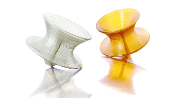 Zwei abstrakte, vasenförmige Glasobjekte in Silber und Gold stehen auf einer reflektierenden Oberfläche.