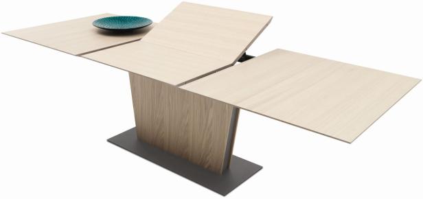 Ein ausziehbarer Esstisch aus hellem Holz mit einer blauen Schale darauf.