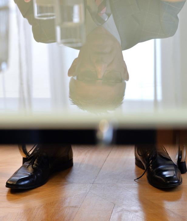 Ein Mann mit Brille sitzt an einem Tisch, von unten durch die Glasplatte fotografiert.