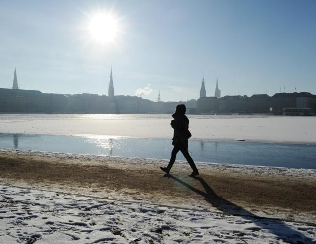 Eine Person geht an der winterlichen Alster in Hamburg entlang.