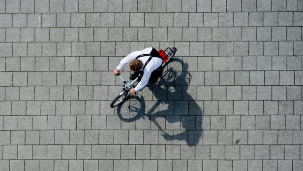 Ein Mann mit Hemd und Hosenträgern fährt mit dem Fahrrad über einen gepflasterten Weg.