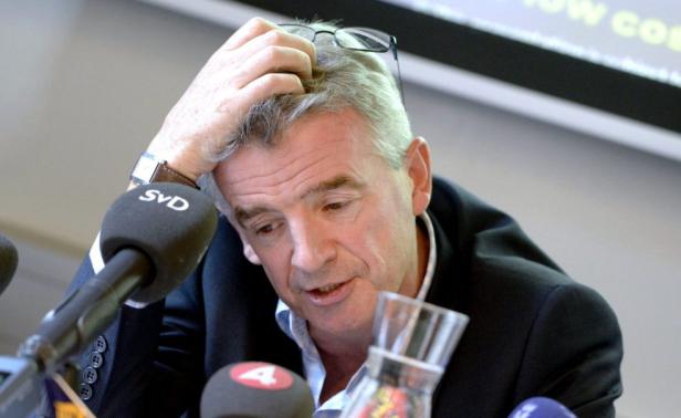 Ein Mann mit Anzug und Brille gestikuliert vor mehreren Mikrofonen.