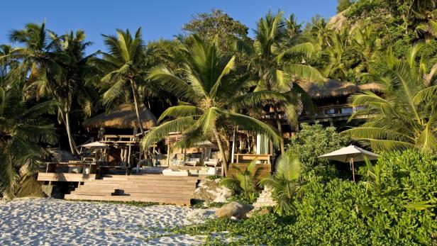 Ein luxuriöses Strandresort mit strohgedeckten Hütten inmitten von Palmen und üppiger Vegetation.