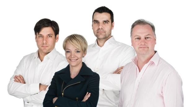 Vier Personen posieren vor einem weißen Hintergrund für ein Gruppenfoto.
