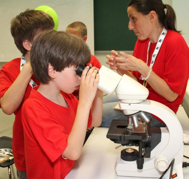 Ein Junge schaut durch ein Mikroskop, während eine Frau ihm Anweisungen gibt.