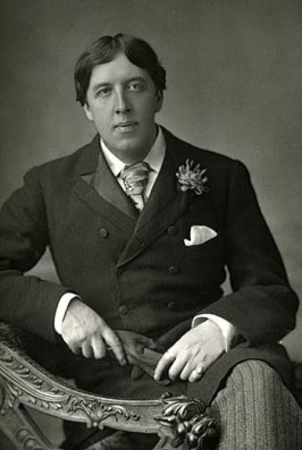 Ein Porträt von Oscar Wilde, sitzend in einem dunklen Anzug mit Blume am Revers.