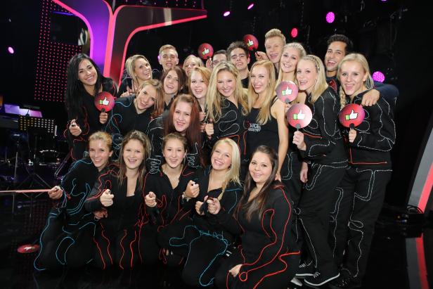 Eine Gruppe junger Tänzerinnen und Tänzer posiert mit „Daumen hoch“-Schildern.