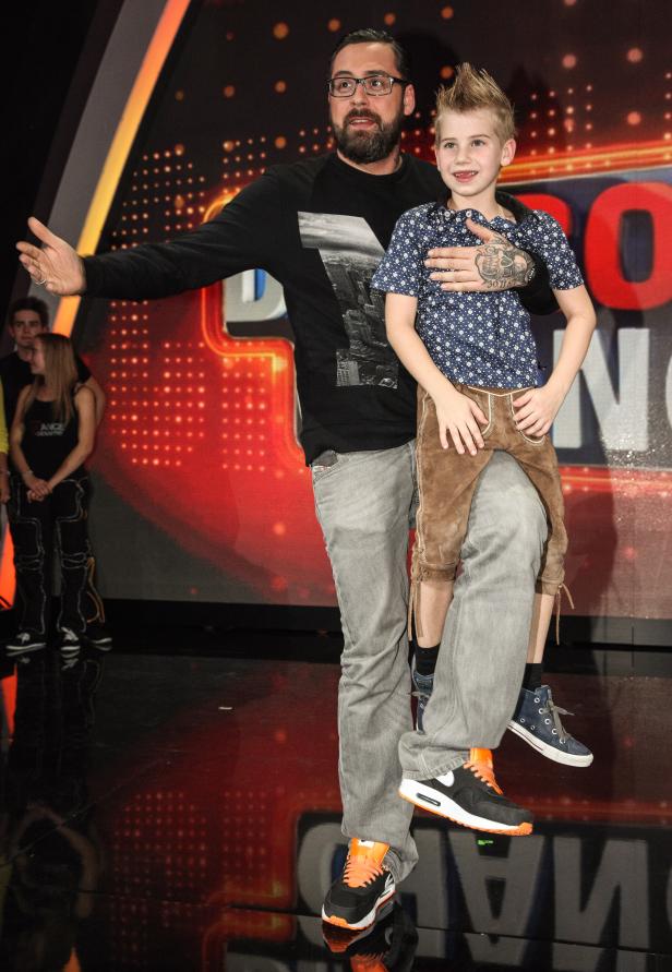 Ein Mann mit Brille hält einen Jungen in Lederhosen auf dem Arm.