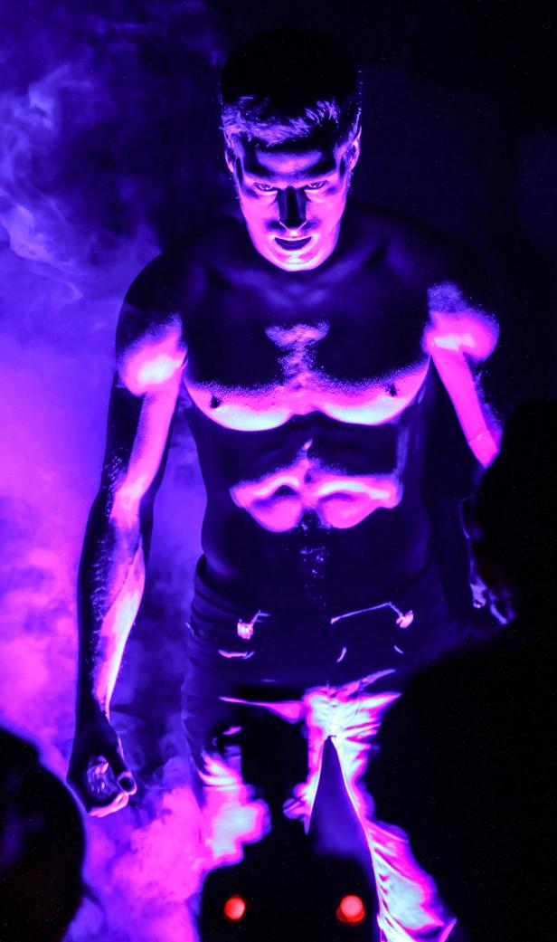 Ein muskulöser Mann steht im violetten Licht und blickt finster in die Kamera.