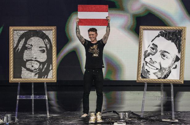 Ein Mann hält eine österreichische Flagge zwischen zwei Porträtgemälden hoch.