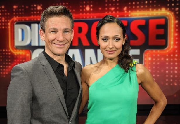 Ein Mann im Anzug und eine Frau in einem grünen Kleid posieren vor dem Logo „Die große Chance“.