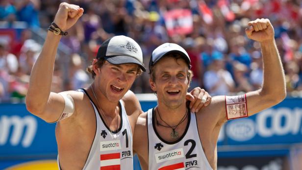 Zwei Beachvolleyballspieler jubeln mit erhobenen Fäusten über ihren Sieg.