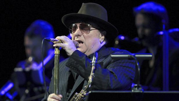 Van Morrison singt mit Hut und Sonnenbrille auf der Bühne, ein Saxophon neben sich.
