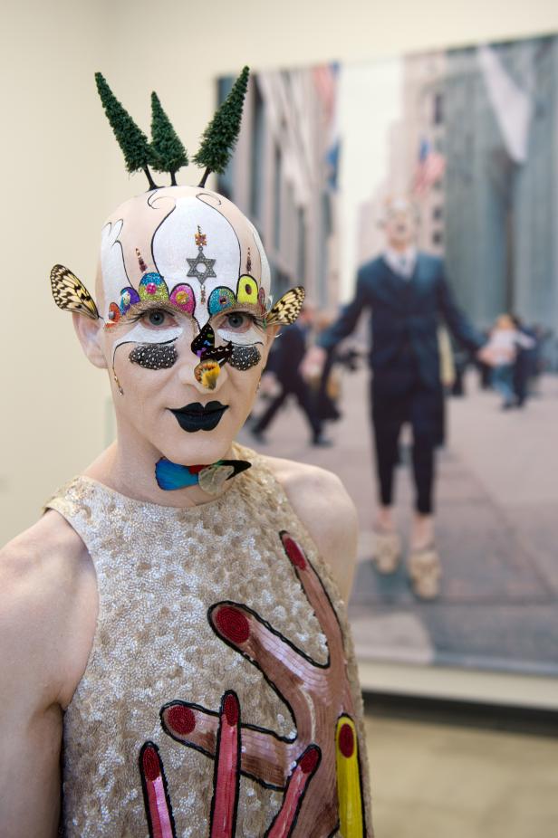 Eine Person mit aufwendigem Make-up und Kopfschmuck steht vor einem unscharfen Hintergrund.