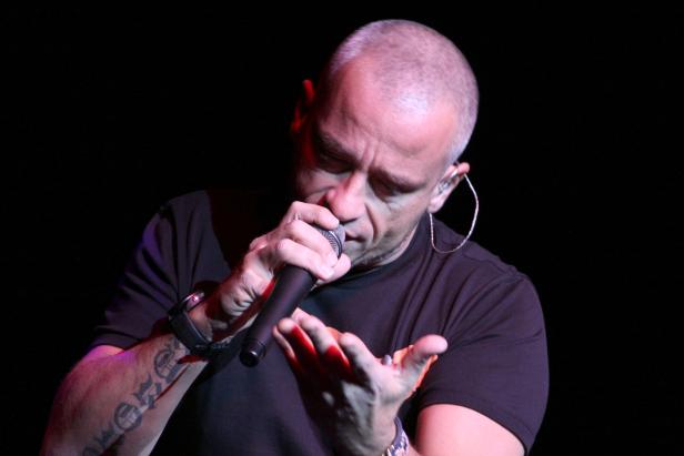 Ein Mann mit Tätowierungen singt in ein Mikrofon.