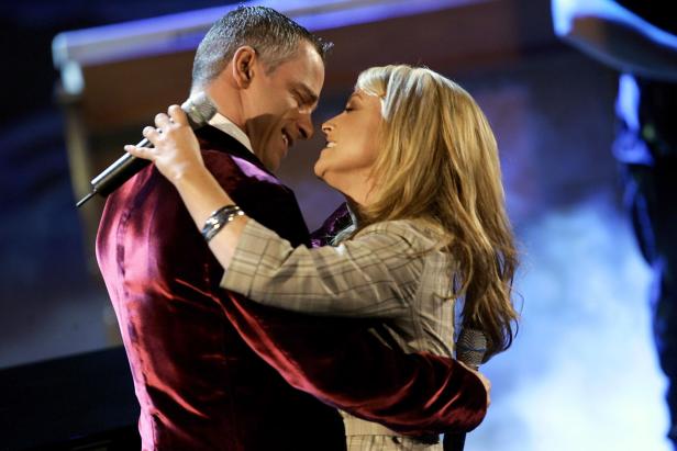 Ein Mann und eine Frau umarmen sich auf einer Bühne und halten Mikrofone.