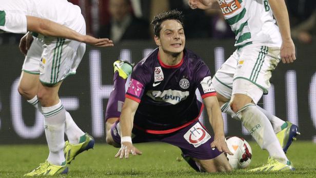 Ein Fußballspieler in lila Uniform liegt auf dem Rasen während eines Spiels.