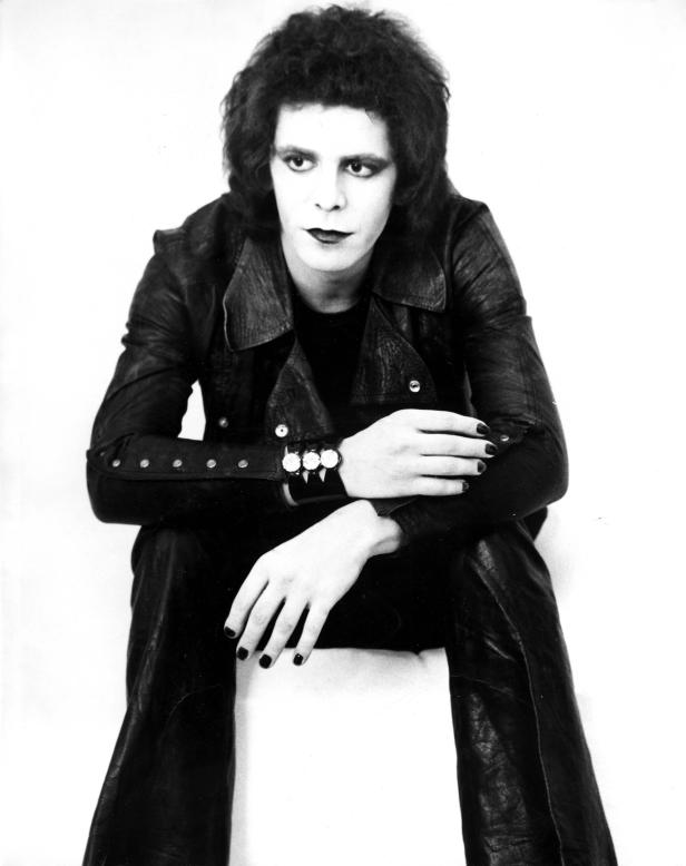 Ein androgynes Model mit dunklem Haar, Lederjacke und dunklem Lippenstift posiert.