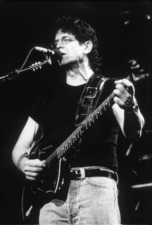Lou Reed spielt Gitarre und singt in ein Mikrofon.