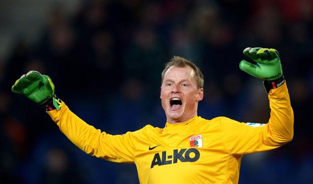 Ein jubelnder Torwart mit gelbem Trikot und grünen Handschuhen reißt die Arme hoch.