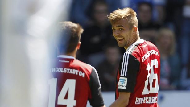 Ein lächelnder Fußballspieler im roten Trikot mit der Nummer 16 blickt über seine Schulter.