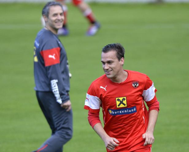 Ein österreichischer Fußballspieler in rotem Trikot mit dem Wappen von Burgenland lächelt.