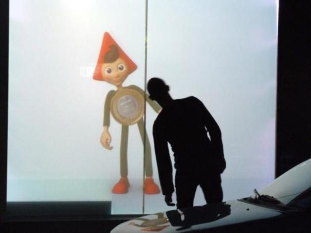 Ein Mann betrachtet im Dunkeln eine Projektion des Maskottchens der Währungseinheit Real, mit einem Kegelhut.