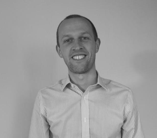 Ein Mann mit Hemd lächelt in die Kamera.