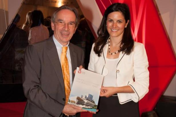 Zwei Personen präsentieren eine Broschüre mit dem Bild eines modernen Gebäudes.