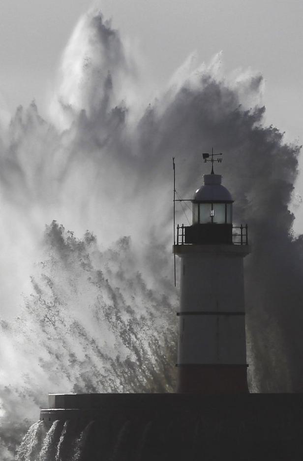 Eine riesige Welle bricht hinter einem Leuchtturm.