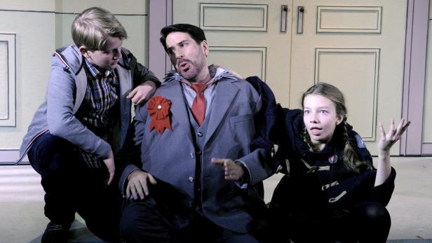 Ein Mann im Anzug mit roter Schleife wird von zwei Kindern gestützt.