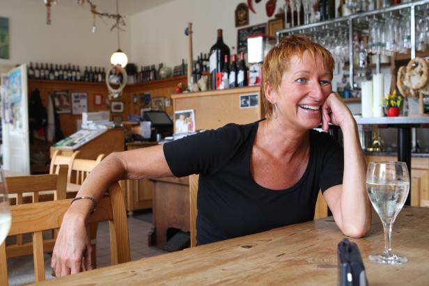 Eine Frau sitzt lächelnd an einem Tisch in einem Restaurant.