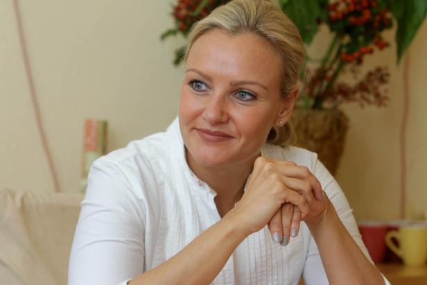 Eine blonde Frau in einem weißen Hemd sitzt und lächelt.
