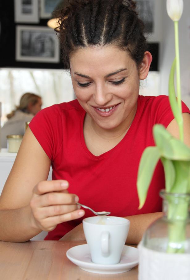 Eine Frau im roten T-Shirt rührt lächelnd in einer Tasse Kaffee.