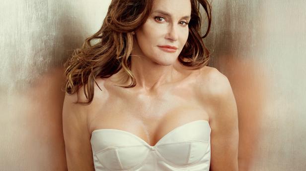 Caitlyn Jenner posiert in einem weißen trägerlosen Oberteil vor einer strukturierten Wand.