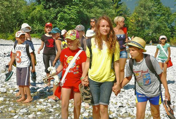 Eine Gruppe Kinder watet barfuß durch einen flachen Fluss.