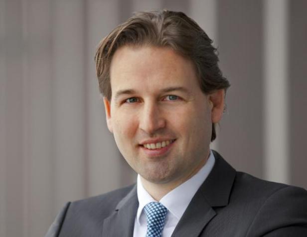 Ein lächelnder Mann im Anzug mit blau gemusterter Krawatte.