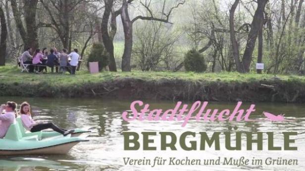 Zwei Frauen fahren mit einem Tretboot auf dem Fluss, im Hintergrund eine Gruppe Menschen am Ufer.