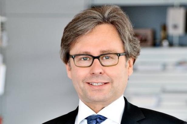 Ein Mann mit Brille und Anzug lächelt in die Kamera.