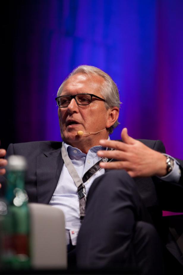 Ein Mann mit Brille und Anzug gestikuliert während einer Präsentation.