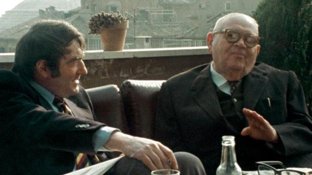 Zwei Männer sitzen auf einer Terrasse und unterhalten sich.