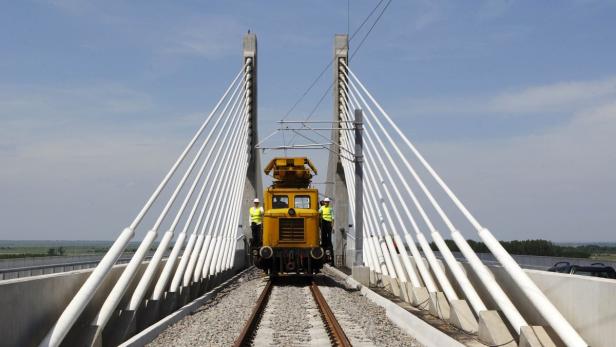 Eine gelbe Lokomotive steht auf einer Brücke mit schrägen, weißen Pfeilern.