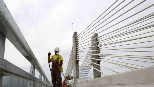 Ein Bauarbeiter streicht auf einer Brücke ein Geländer.