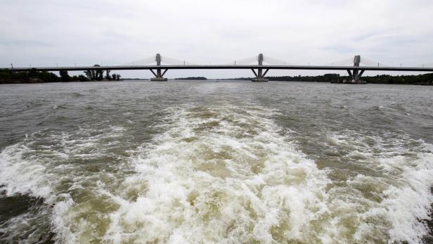 Das Kielwasser eines Bootes führt unter einer Brücke hindurch.