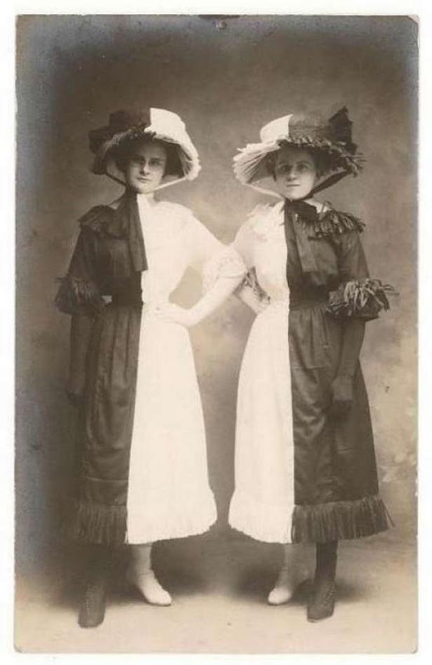 Zwei Frauen in schwarz-weißen Kleidern und Hüten posieren nebeneinander.